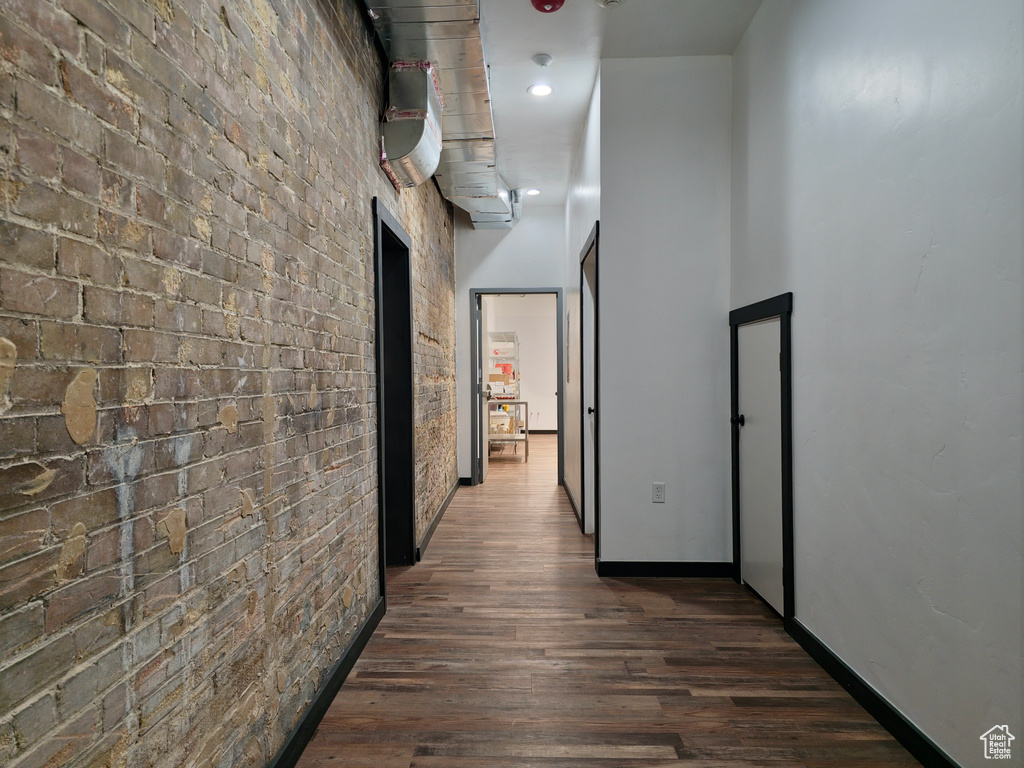 Hallway featuring brick wall, dark wood-style flooring, baseboards, and recessed lighting