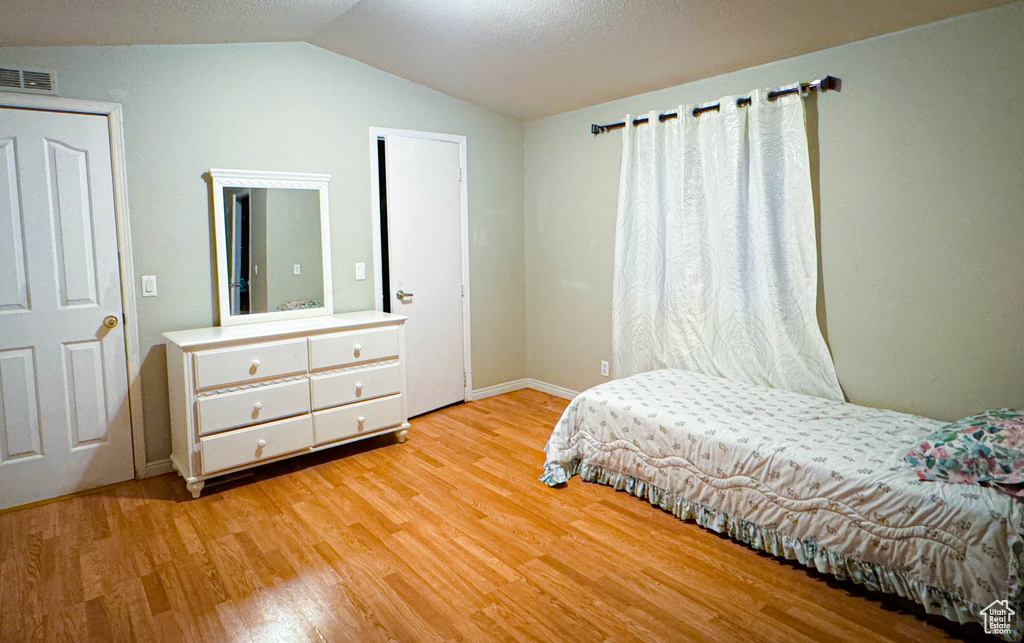 Bedroom featuring baseboards, light wood-style flooring, visible vents, and vaulted ceiling