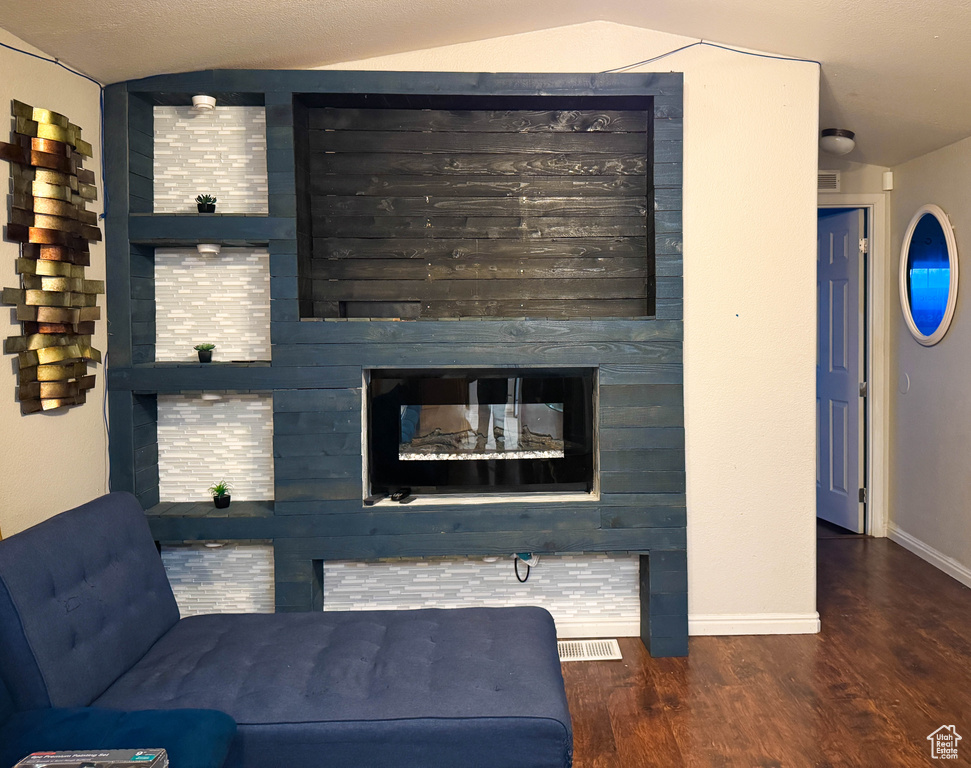 Living area with baseboards, visible vents, vaulted ceiling, a fireplace, and wood finished floors