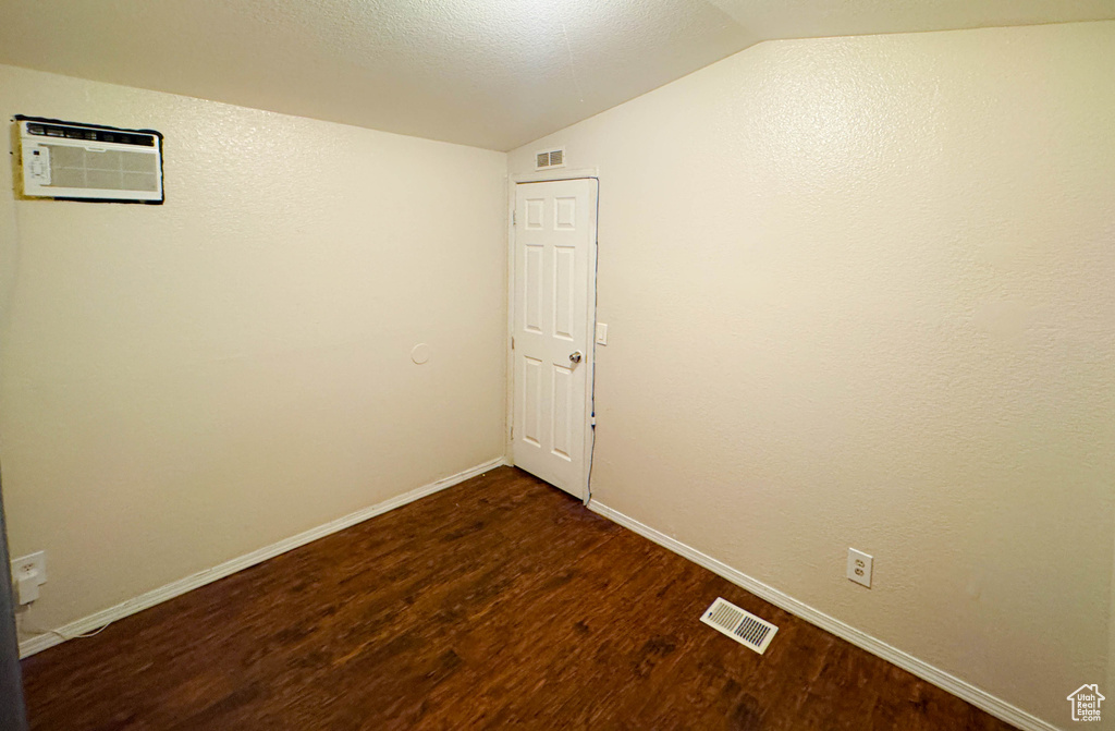 Empty room featuring vaulted ceiling, dark wood-style flooring, a wall mounted AC, and visible vents