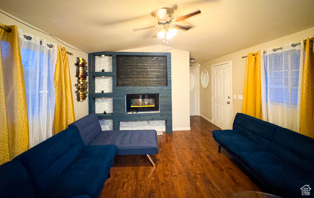 Living area featuring vaulted ceiling, baseboards, ceiling fan, wood finished floors, and a fireplace