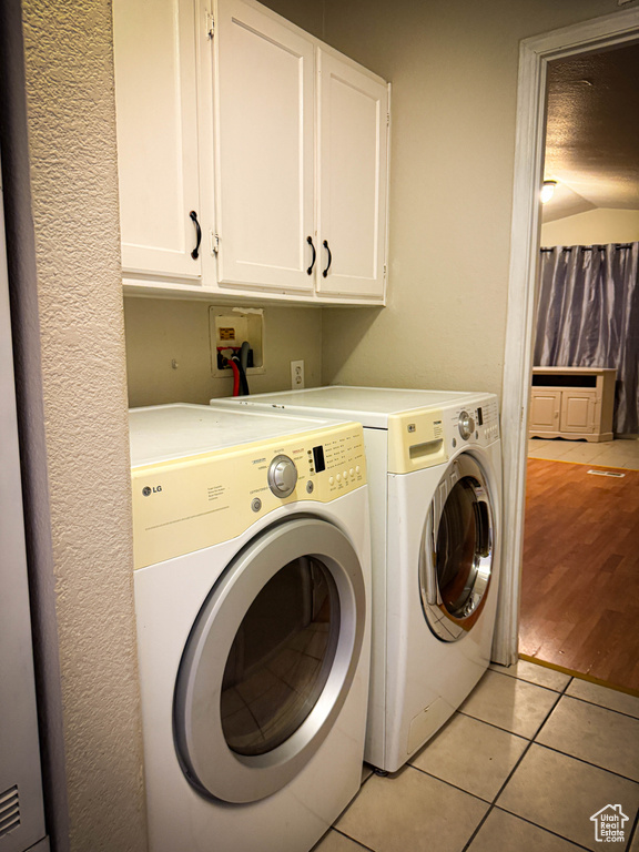 Washroom with light tile patterned floors, a textured ceiling, washing machine and dryer, and cabinet space