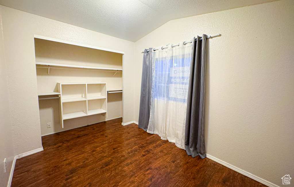 Empty room with baseboards, wood finished floors, lofted ceiling, and a textured wall