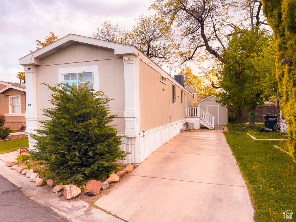 View of property exterior featuring an outdoor structure, driveway, a lawn, and a storage unit