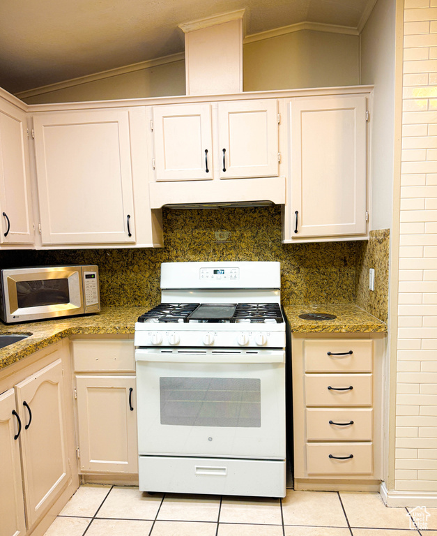 Kitchen featuring under cabinet range hood, crown molding, light tile patterned flooring, and white appliances
