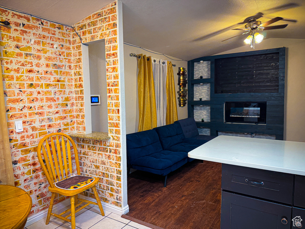 Tiled living room featuring a textured ceiling, vaulted ceiling, a fireplace, and a ceiling fan