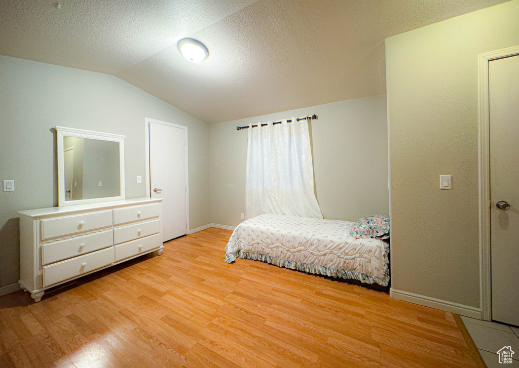 Bedroom with lofted ceiling, a textured ceiling, baseboards, and wood finished floors