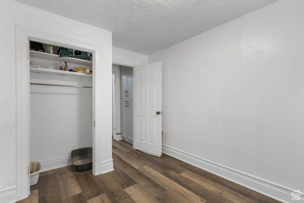 Unfurnished bedroom with baseboards, a closet, a textured ceiling, and dark wood-type flooring