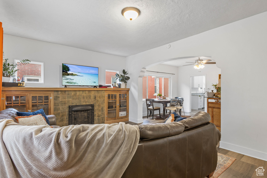 Living room featuring wood finished floors, a fireplace, arched walkways, a ceiling fan, and baseboards
