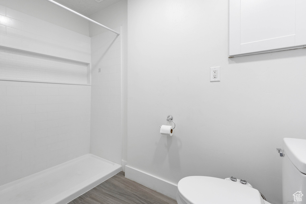 Bathroom featuring toilet, baseboards, wood finished floors, and a shower stall