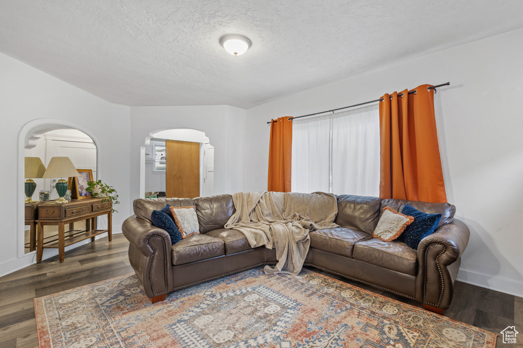 Living area with a textured ceiling, wood finished floors, baseboards, and arched walkways