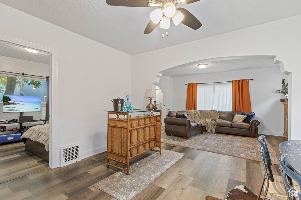 Living room with wood finished floors, visible vents, arched walkways, a ceiling fan, and baseboards