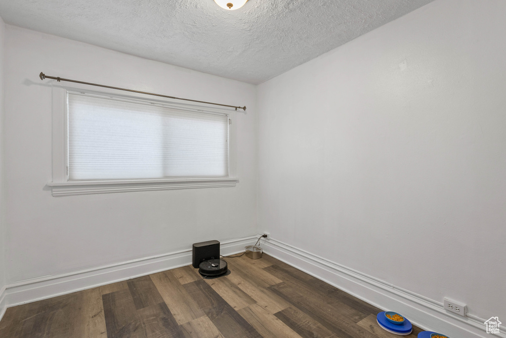 Unfurnished room with a textured ceiling, wood finished floors, and baseboards