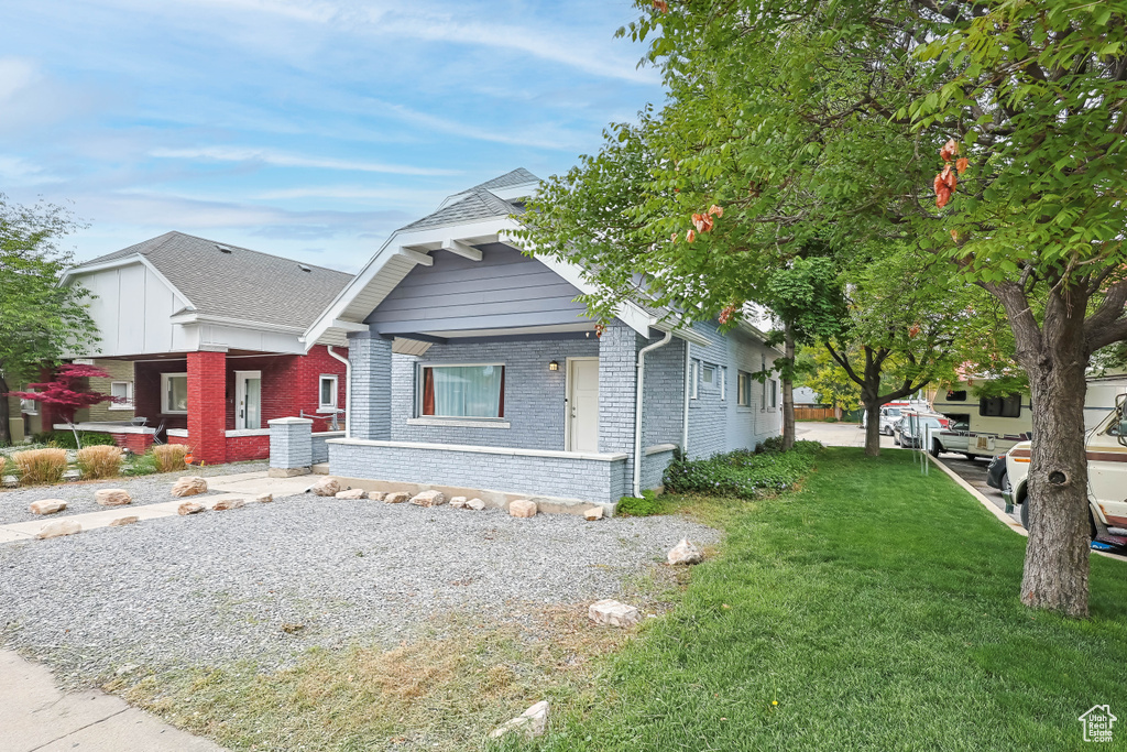 View of front of home with roof with shingles, a front lawn, and brick siding