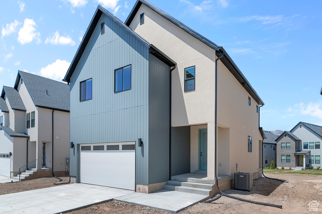 View of front facade featuring cooling unit, concrete driveway, an attached garage, and a residential view