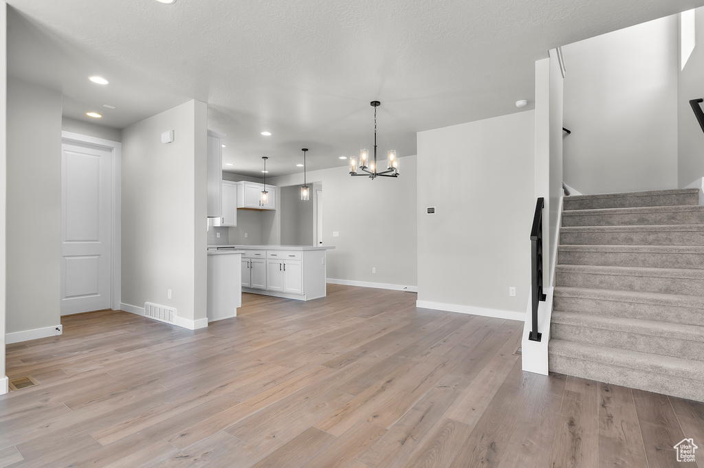 Unfurnished living room featuring a chandelier, stairs, recessed lighting, light wood-type flooring, and baseboards