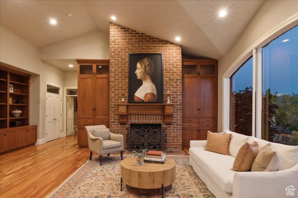 Living room with a brick fireplace, light wood finished floors, recessed lighting, and vaulted ceiling