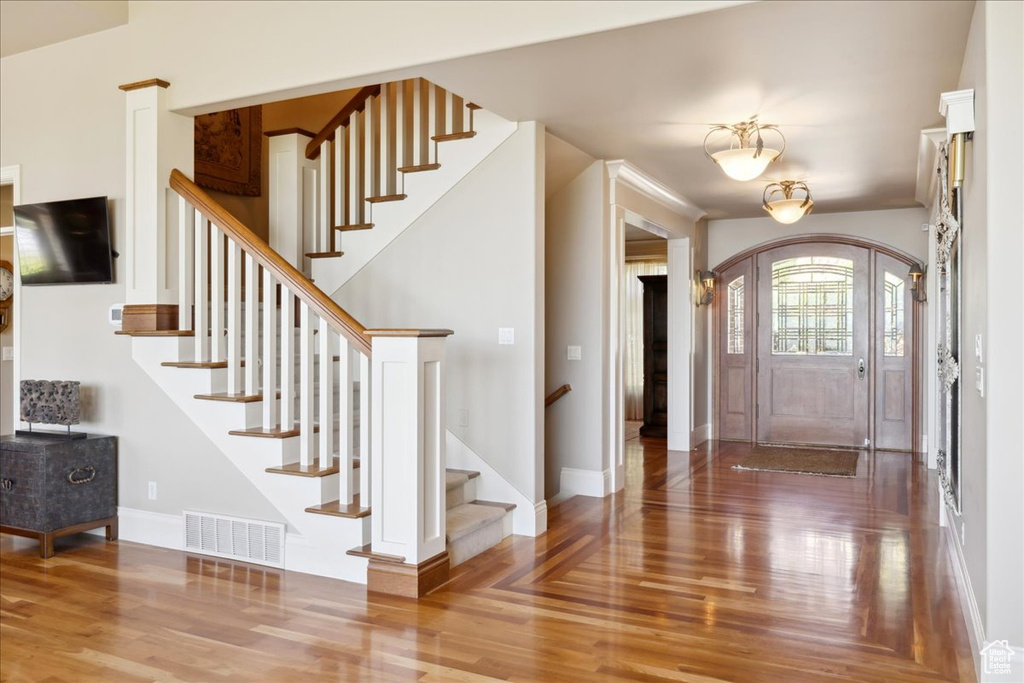 Foyer entrance with stairs, arched walkways, visible vents, and wood finished floors