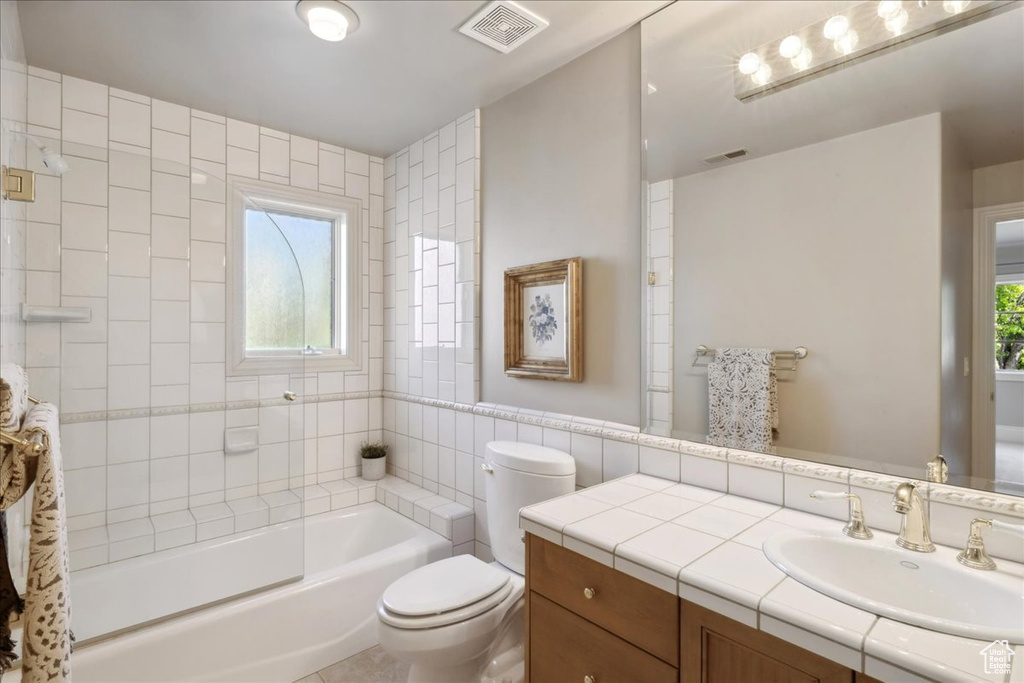 Full bathroom with tile walls, toilet, visible vents, and vanity