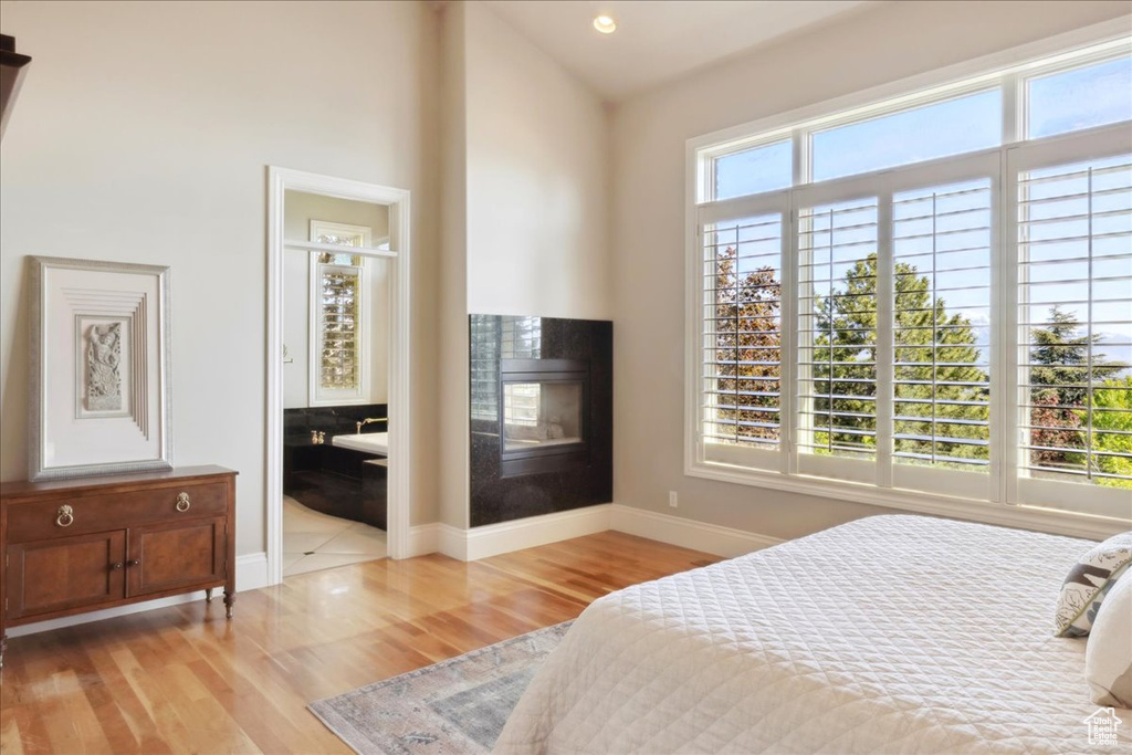 Bedroom featuring ensuite bathroom, vaulted ceiling, light wood-style flooring, baseboards, and a multi sided fireplace