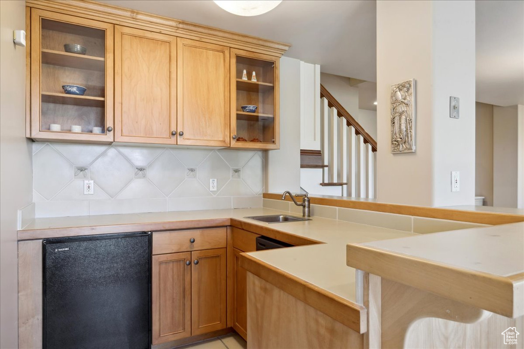 Kitchen featuring a sink, a peninsula, black refrigerator, decorative backsplash, and light countertops