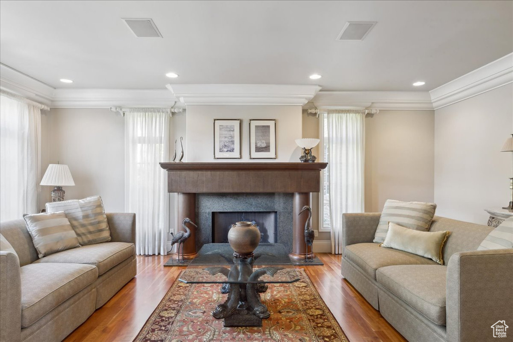 Living room featuring visible vents, wood finished floors, a fireplace with raised hearth, and ornamental molding