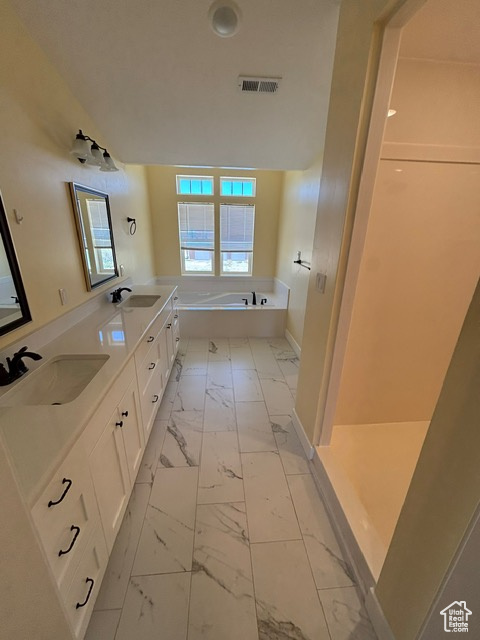 Bathroom featuring marble finish floors, a garden tub, baseboards, and double vanity