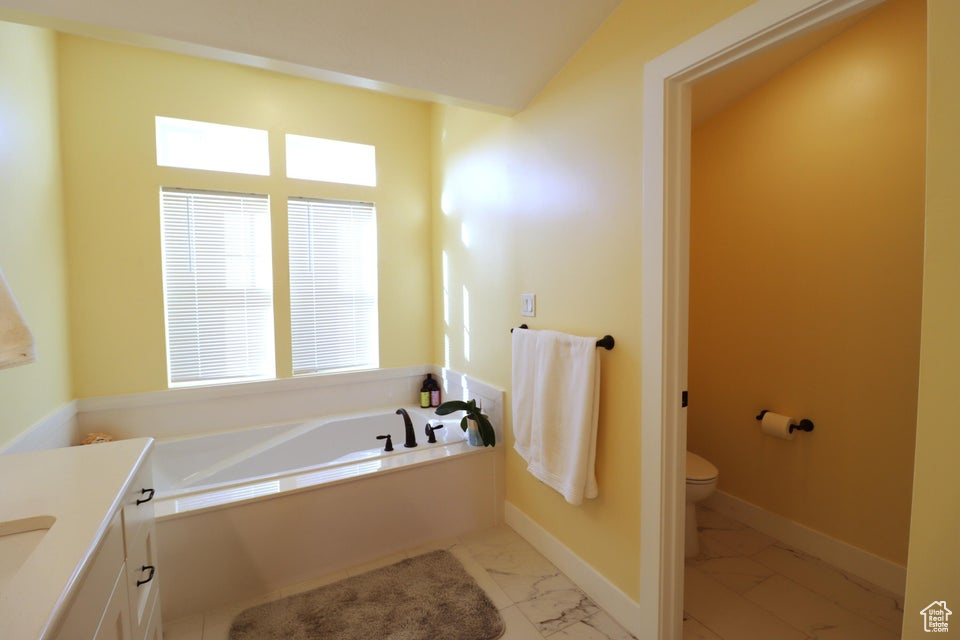 Bathroom with marble finish floor, toilet, a bath, and plenty of natural light
