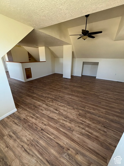Bonus room with vaulted ceiling, a ceiling fan, dark wood-style flooring, a textured ceiling, and baseboards