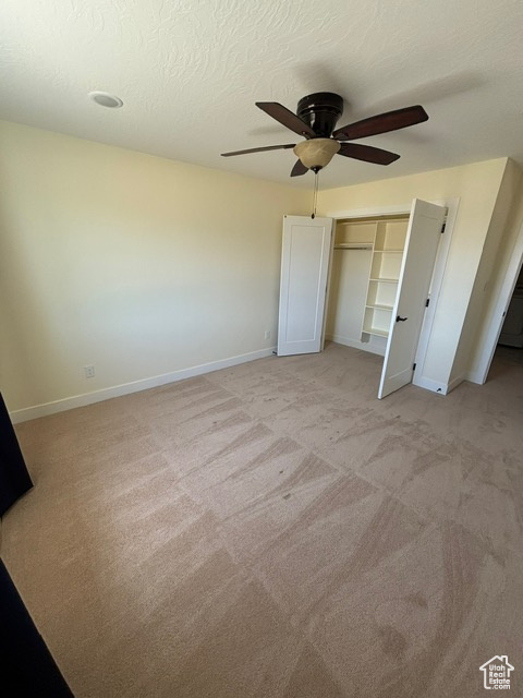 Unfurnished bedroom featuring baseboards, light carpet, a closet, a ceiling fan, and a textured ceiling