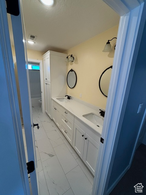 Bathroom featuring marble look tile flooring, double vanity, toilet, and a textured ceiling