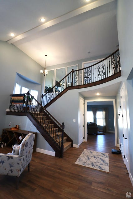 Entryway featuring wood finished floors, stairway, an inviting chandelier, a high ceiling, and baseboards