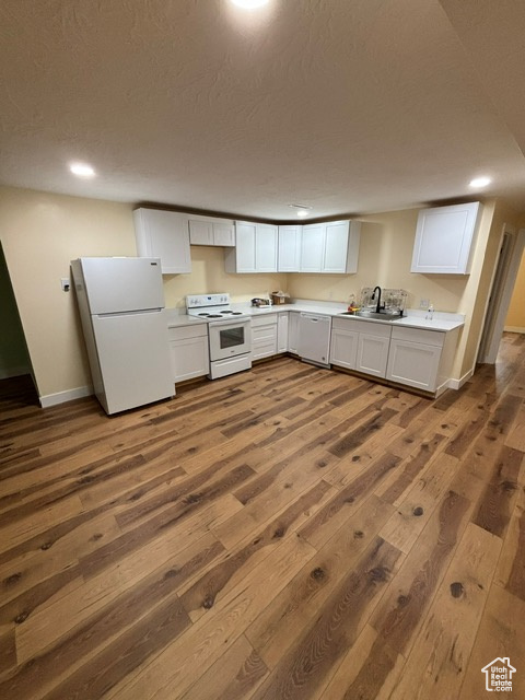 Kitchen featuring white appliances, dark wood finished floors, baseboards, light countertops, and white cabinetry