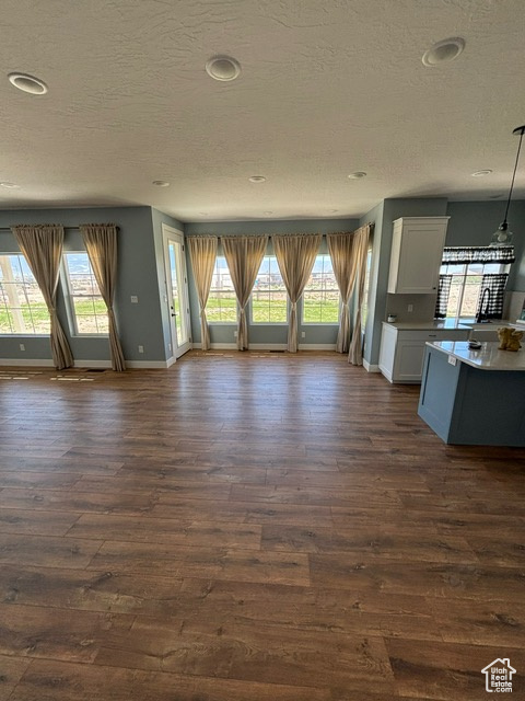 Unfurnished living room featuring a textured ceiling, dark wood-style flooring, plenty of natural light, baseboards, and recessed lighting