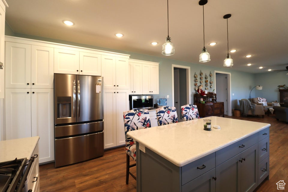 Kitchen with decorative light fixtures, appliances with stainless steel finishes, dark wood-style floors, and white cabinetry