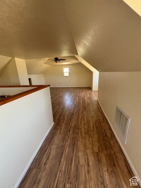 Additional living space with a textured ceiling, dark wood-type flooring, vaulted ceiling, ceiling fan, and baseboards