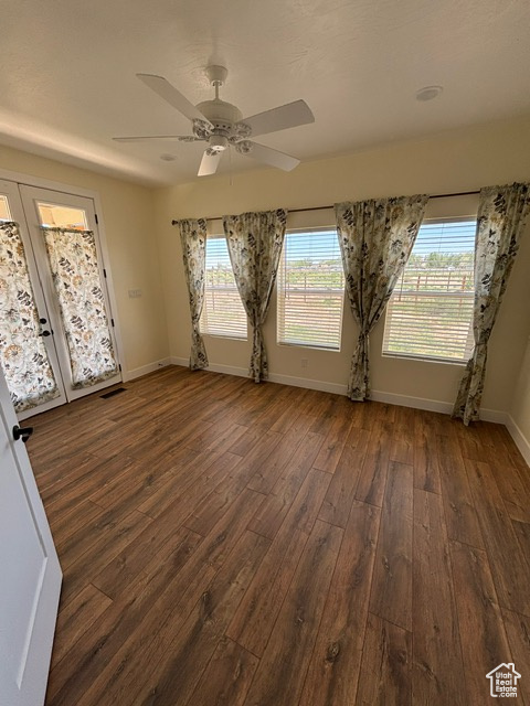 Empty room featuring dark wood-type flooring, baseboards, healthy amount of natural light, and a ceiling fan