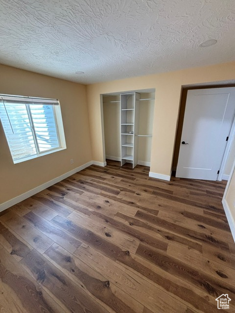 Unfurnished bedroom featuring wood finished floors, a textured ceiling, a closet, and baseboards