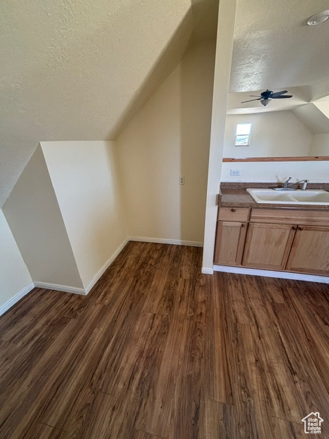 Bonus room featuring a sink, a textured ceiling, lofted ceiling, dark wood-style floors, and a ceiling fan