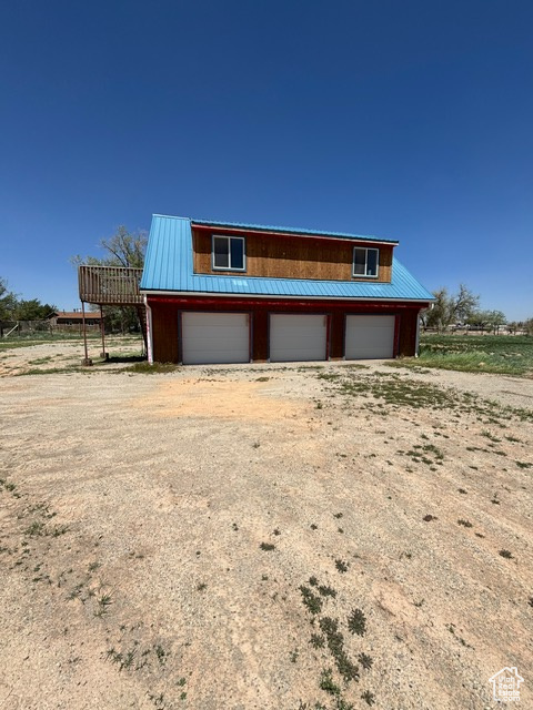 View of front facade featuring a garage, metal roof, and dirt driveway