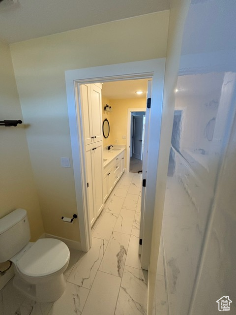 Bathroom featuring marble finish flooring, toilet, baseboards, and vanity