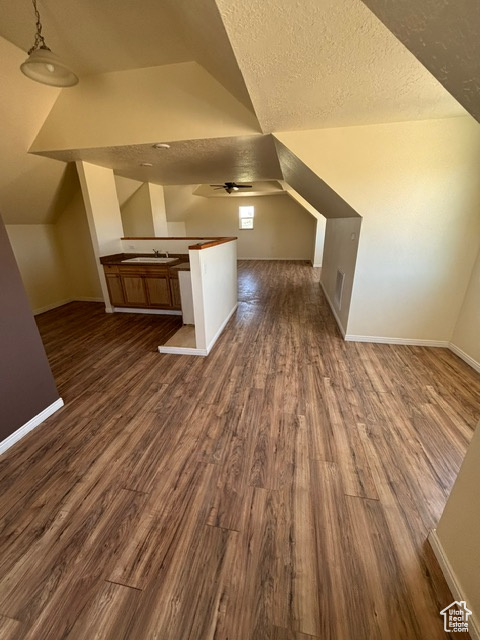 Additional living space featuring dark wood-style flooring, vaulted ceiling, baseboards, a textured ceiling, and a ceiling fan