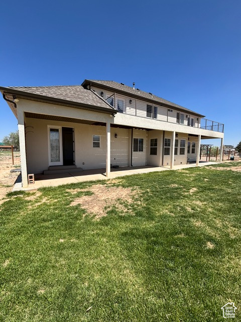 Rear view of property featuring a patio, a lawn, stucco siding, and a balcony
