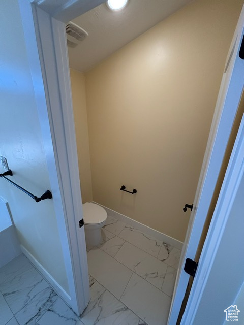 Bathroom featuring marble finish floors, toilet, and baseboards