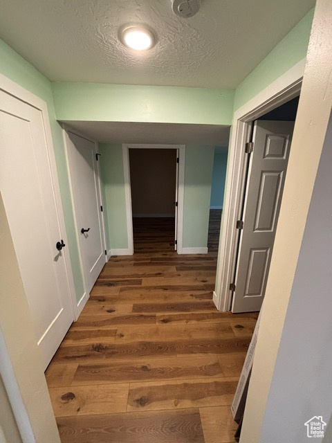 Hallway featuring wood finished floors, a textured ceiling, and baseboards