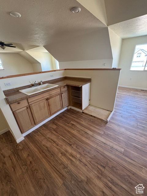 Kitchen featuring a textured ceiling, a sink, dark wood-type flooring, baseboards, and light brown cabinetry