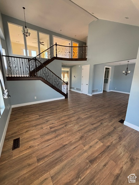 Unfurnished living room with a chandelier, wood finished floors, baseboards, high vaulted ceiling, and stairway