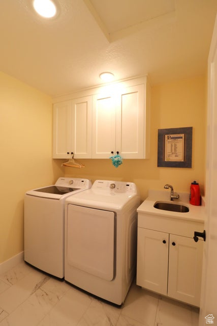 Washroom featuring baseboards, marble finish floor, a sink, washing machine and clothes dryer, and cabinet space