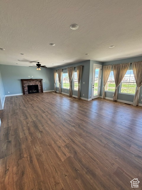 Unfurnished living room featuring a textured ceiling, baseboards, and dark wood-style flooring