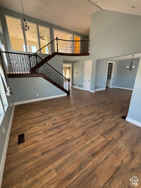 Unfurnished living room featuring a chandelier, wood finished floors, baseboards, high vaulted ceiling, and stairs